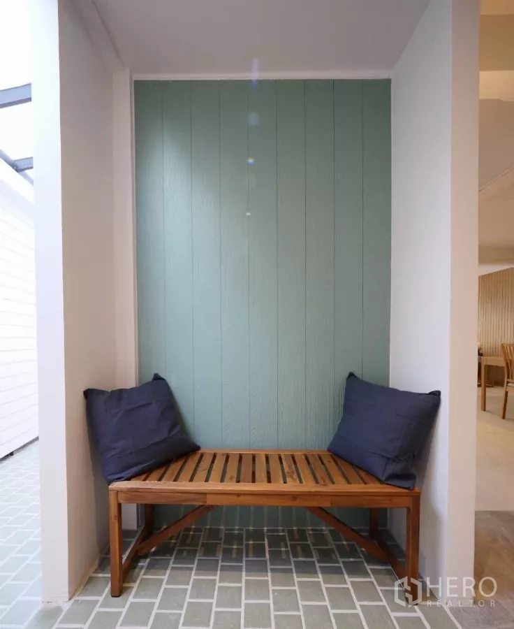 Townhouse for rent or sale in Watthana, Bangkok - Small patio nook featuring a wooden bench and teal feature wall.