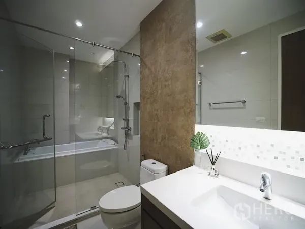 Condominium for rent in Khlong Toei, Bangkok - Contemporary bathroom with glass shower and bathtub, vanity and large mirror.