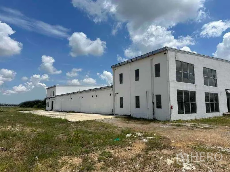 Warehouse for rent in Sai Noi, Nonthaburi - Side elevation of long-span warehouse and two-storey office with wide yard for truck maneuvering.