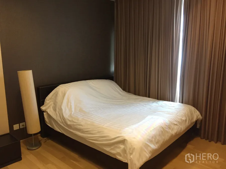 Condominium for rent in Khlong Toei, Bangkok - Primary bedroom with double bed, wood flooring, floor lamp and blackout curtains in a Khlong Toei condo.