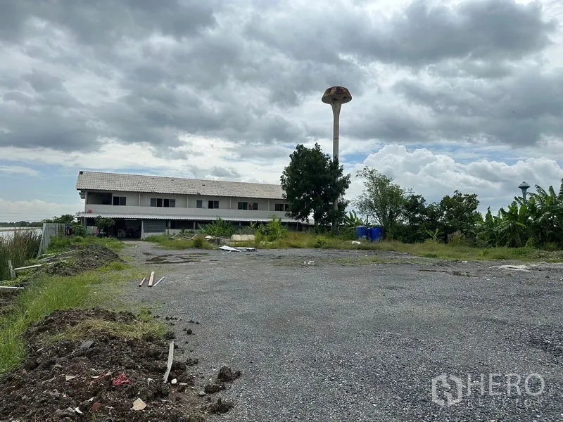 Factory for rent in Lam Luk Ka, Pathum Thani - Gravel yard and ancillary building with water tower view in the background.