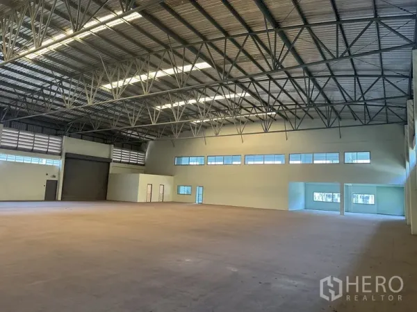 Factory for rent in Chon Buri - Warehouse interior with roller shutter door, windows and adjoining office block.