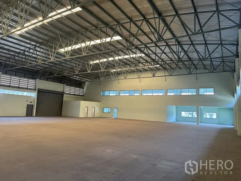 Factory for rent in Chon Buri - Warehouse interior with roller shutter door, windows and adjoining office block.