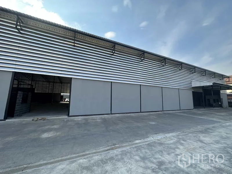 Warehouse for rent in Lam Luk Ka, Pathum Thani - Side facade with horizontal metal cladding and multiple sliding doors along the loading frontage.