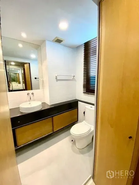 Condominium for rent in Chatuchak, Bangkok - Modern bathroom with vessel sink, large mirror, and a window with wooden blinds.