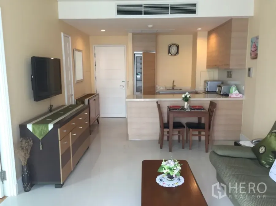 Condominium for rent or sale in Khlong Toei, Bangkok - Bright open-plan living room with wall-mounted TV, breakfast bar kitchen and a small dining table.