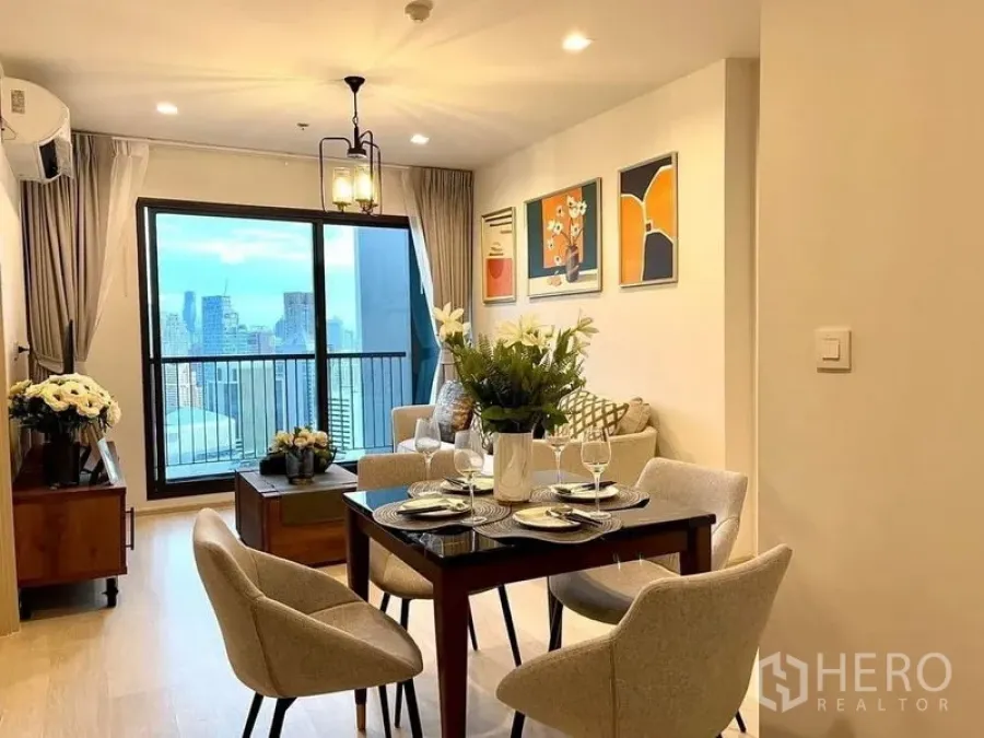 Condominium for rent in Pathum Wan, Bangkok - Dining area set for four with flowers and tableware opening to living room and balcony view.
