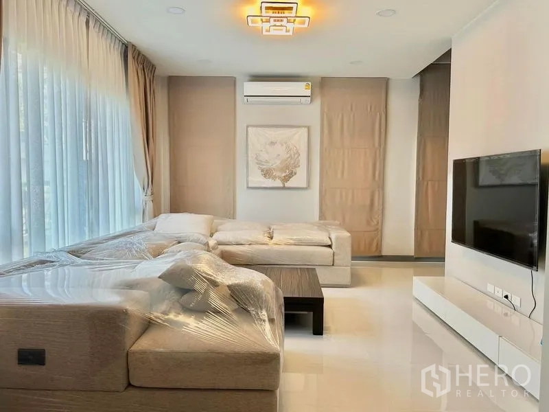 Detached House for rent - Bright living room with L-shaped sofa, TV wall and floor-to-ceiling windows.