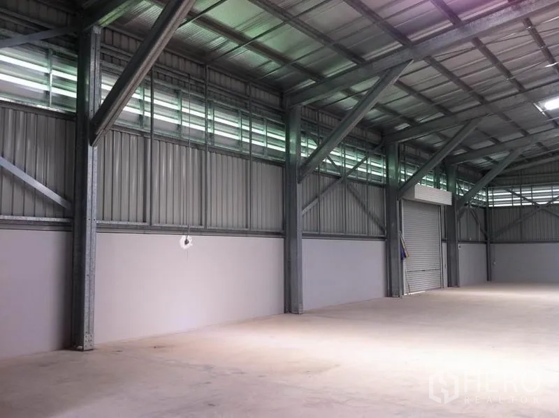 Warehouse for rent in Sai Mai, Bangkok - Open warehouse bay showing steel columns, clerestory windows for natural light, smooth concrete floor and roll‑up loading door.