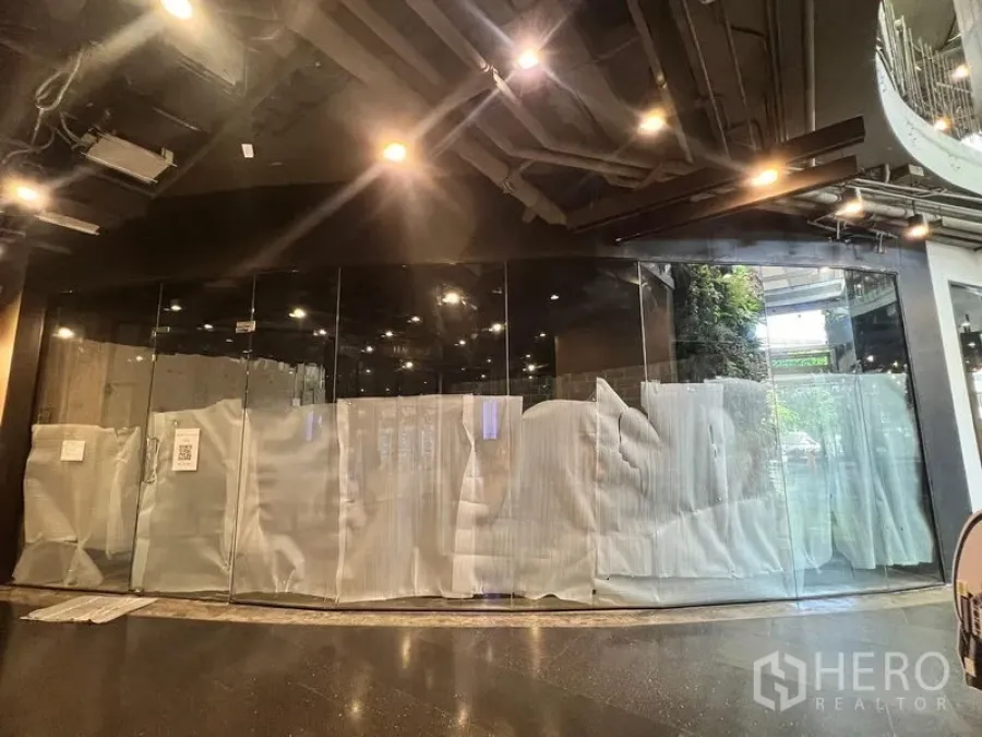 Retail Space for rent - Wide view of the glass façade with curved corner, black ceiling with downlights, and greenery visible outside.