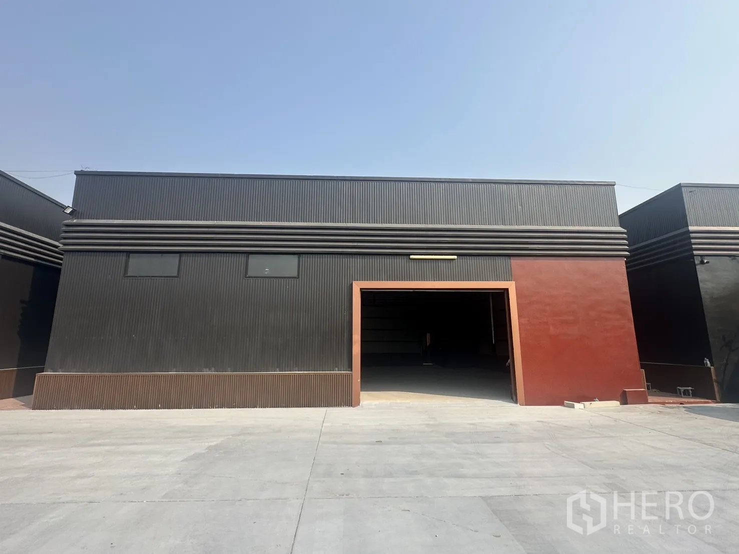 Warehouse for rent in Prawet, Bangkok - Modern black warehouse exterior in Prawet, Bangkok with a wide vehicle entrance and large concrete forecourt.