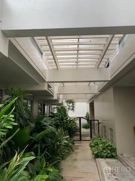 联排别墅 出租在Khlong Toei, Bangkok - 天窗覆盖的庭院走廊，被葱郁绿植与黑色大门环绕。