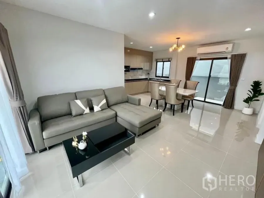 Townhouse for rent in Bang Phli, Samut Prakan - Bright open-plan living room with L-shaped sofa, marble dining table, beige kitchen and sliding glass doors in a Bang Phli townhouse.