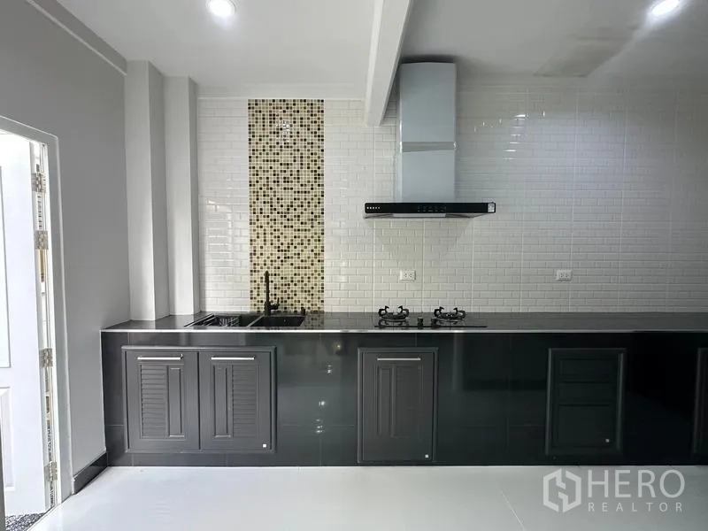 Detached House for sale in Lam Luk Ka, Pathum Thani - Built-in kitchen with black cabinets, gas hob, range hood and subway-tile backsplash.