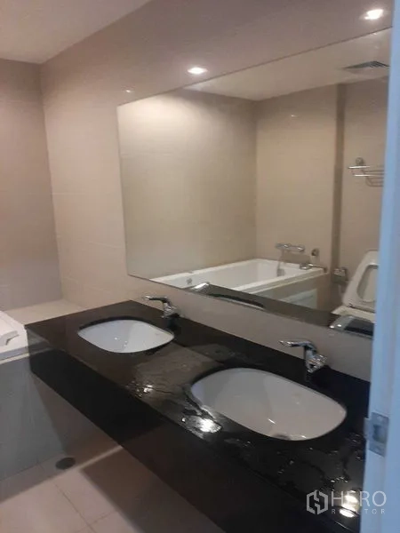 Condominium for rent or sale in Huai Khwang, Bangkok - Bathroom featuring a black countertop double vanity, large mirror, bathtub and toilet.