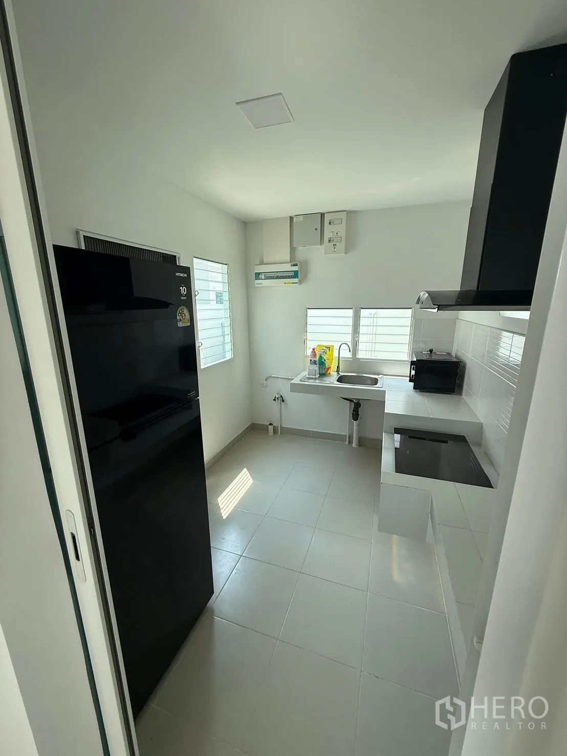 Detached House for rent in Bang Phli, Samut Prakan - Enclosed kitchen with a refrigerator, sink, built-in cooktop, range hood, and tiled floor.