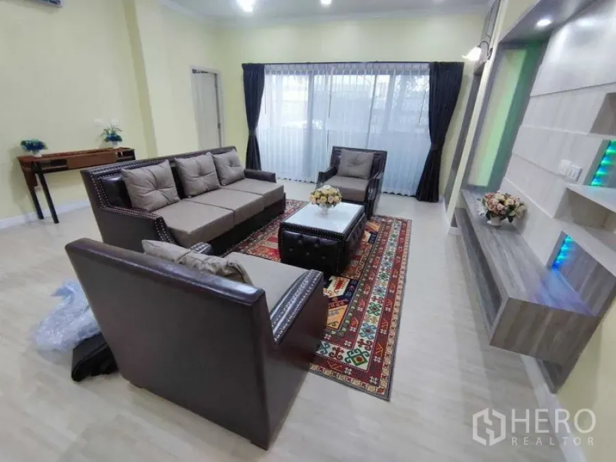 Condominium for rent in Khlong Toei, Bangkok - Spacious living room at President Park condo with leather sofa set, media wall shelving, patterned rug and large curtained window.