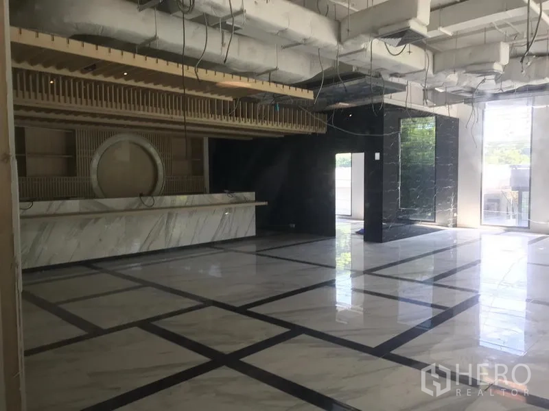 Retail Space for rent in Khlong Toei, Bangkok - Spacious retail interior with marble-look floors, high ceiling, exposed ducts, and a long stone counter beside full-height windows.