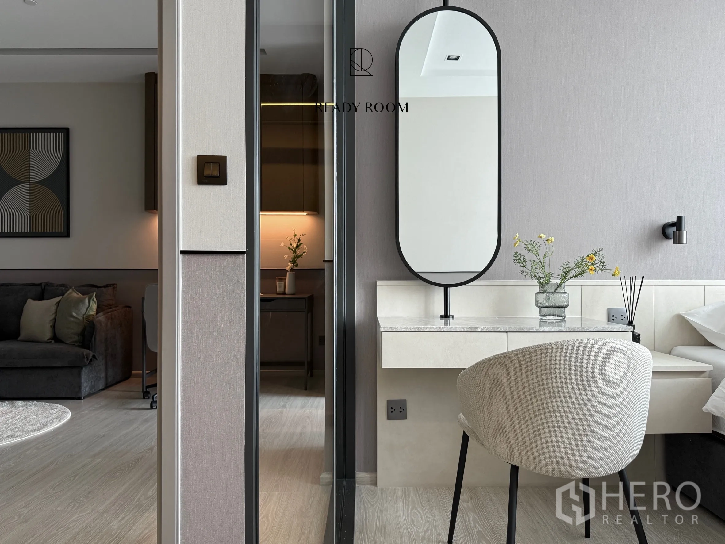 Condominium for rent in Khlong Toei, Bangkok - Bedroom vanity with oval mirror and chair beside a sliding door to the living room.