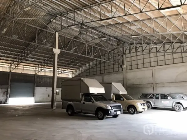 Warehouse for rent in Mueang Samut Prakan, Samut Prakan - Interior view toward roller shutters with steel truss ceiling, smooth concrete floor, and ample vehicle space.