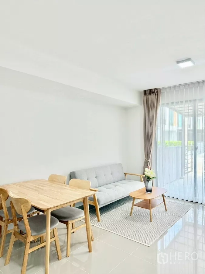 Townhouse for rent in Bang Phli, Samut Prakan - Dining table beside sofa in airy lounge with floor-to-ceiling windows.