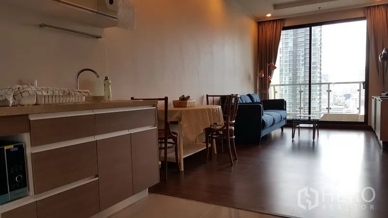 Condominium for rent in Sathon, Bangkok - Open-plan living room with kitchenette, dining set, blue sofa and balcony overlooking the Sathorn skyline.