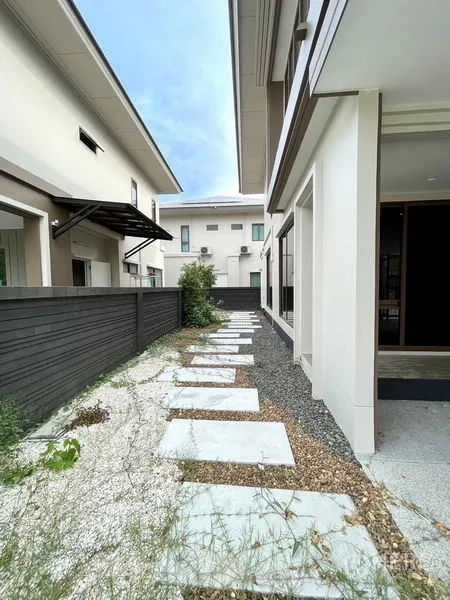Detached House for sale in Bang Kapi, Bangkok - Rear side garden walkway with stone pavers, gravel and privacy fence beside the home exterior.