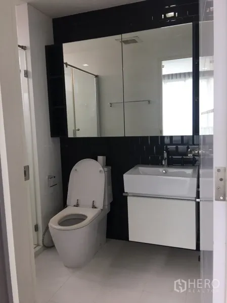 Condominium for sale in Phra Khanong, Bangkok - Contemporary bathroom with mirrored cabinet, square vanity, toilet and a glass-enclosed shower.