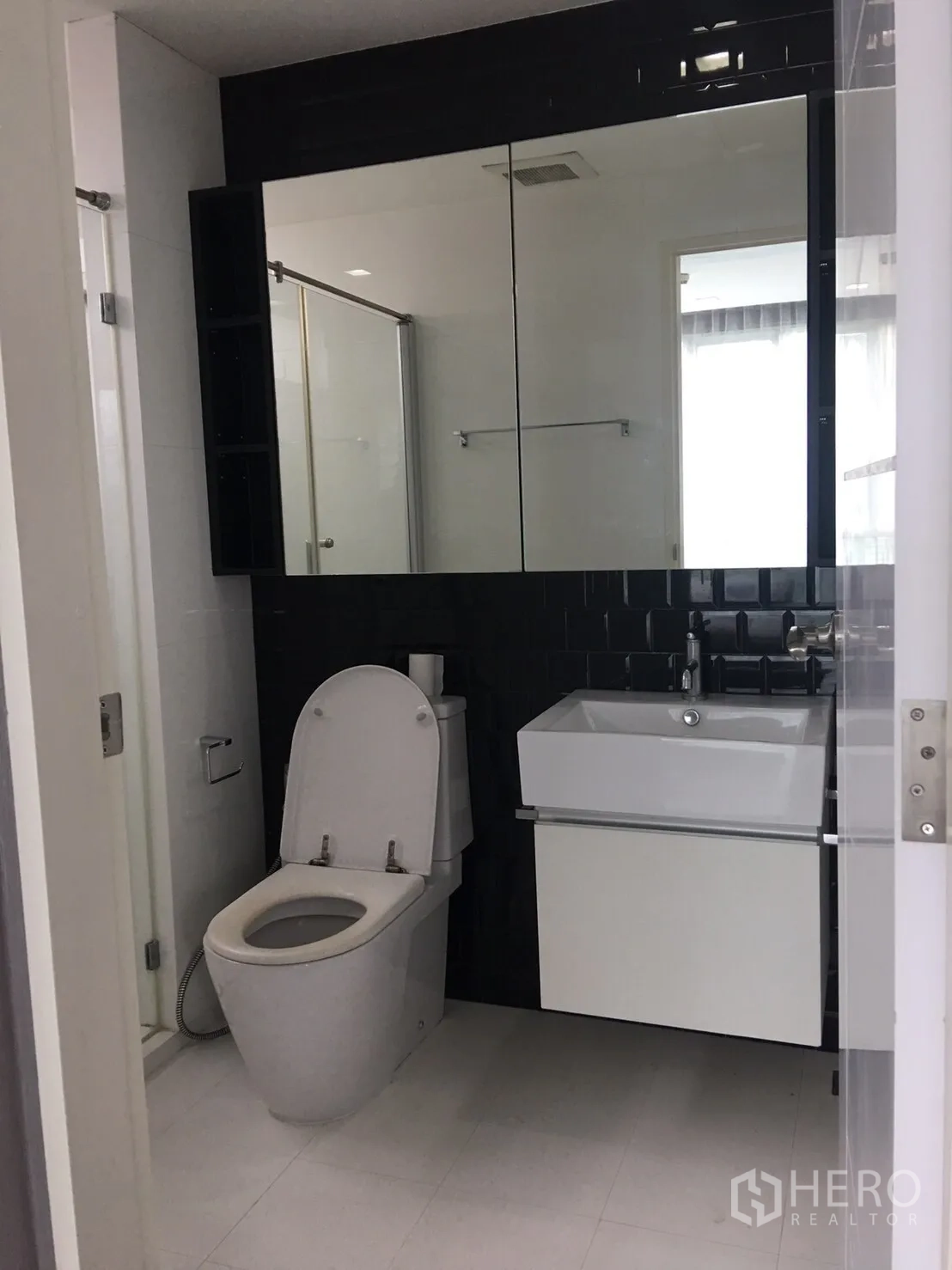 Condominium for sale in Phra Khanong, Bangkok - Contemporary bathroom with mirrored cabinet, square vanity, toilet and a glass-enclosed shower.