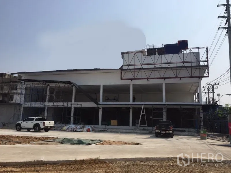 货栈 出租在Bang Kapi, Bangkok - 两层白色仓库在施工中，设有大面积玻璃开口、脚手架与宽阔混凝土场地。