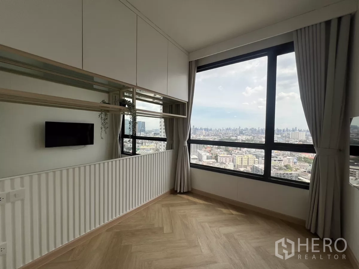 Condominium for rent or sale in Chatuchak, Bangkok - Second bedroom or study with wide picture window, mirrored cabinets and wall‑mounted TV overlooking the city.