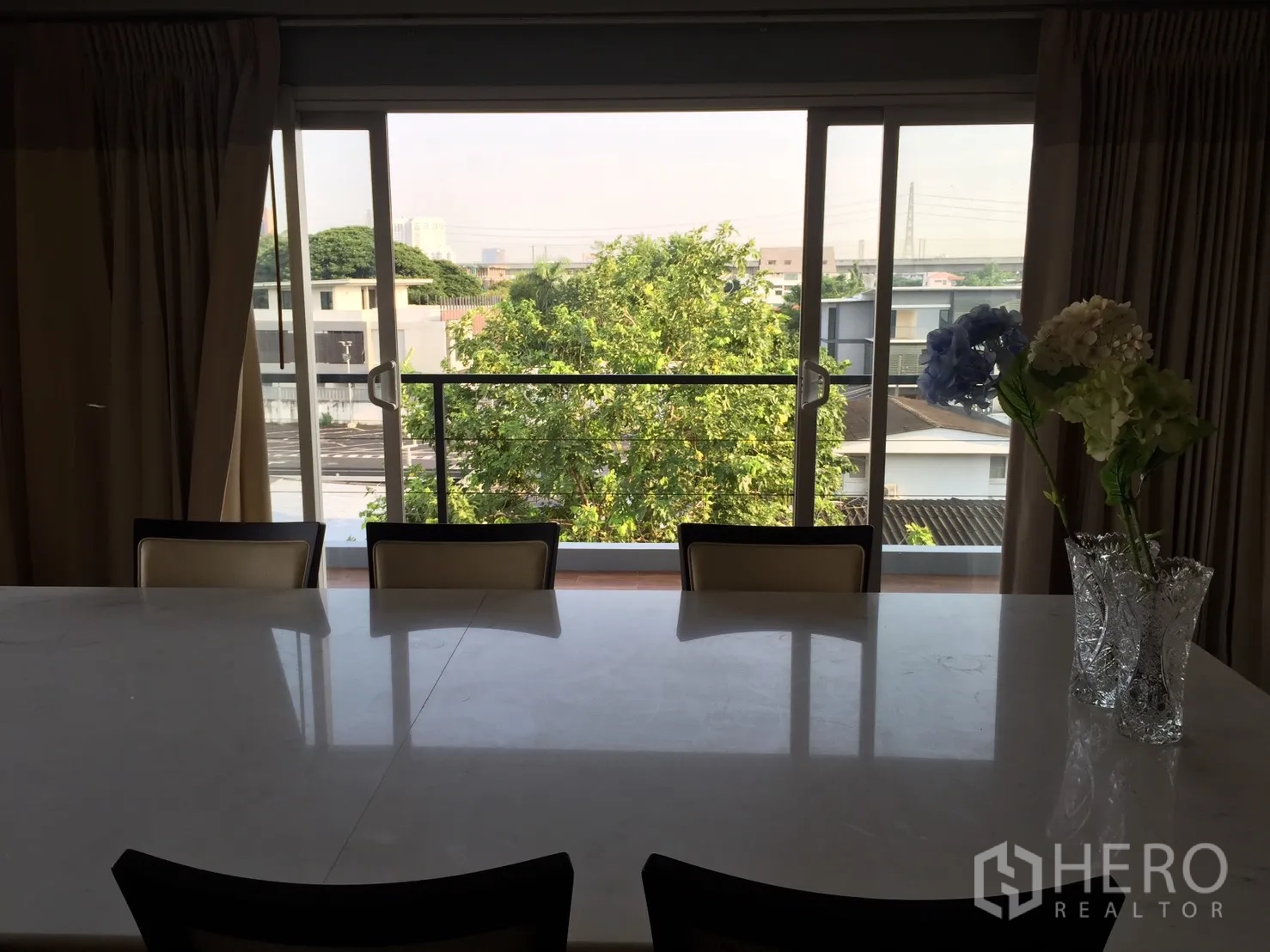 Home Office for rent or sale in Suan Luang, Bangkok - Dining area with a marble table facing sliding glass doors and a balcony with leafy views.