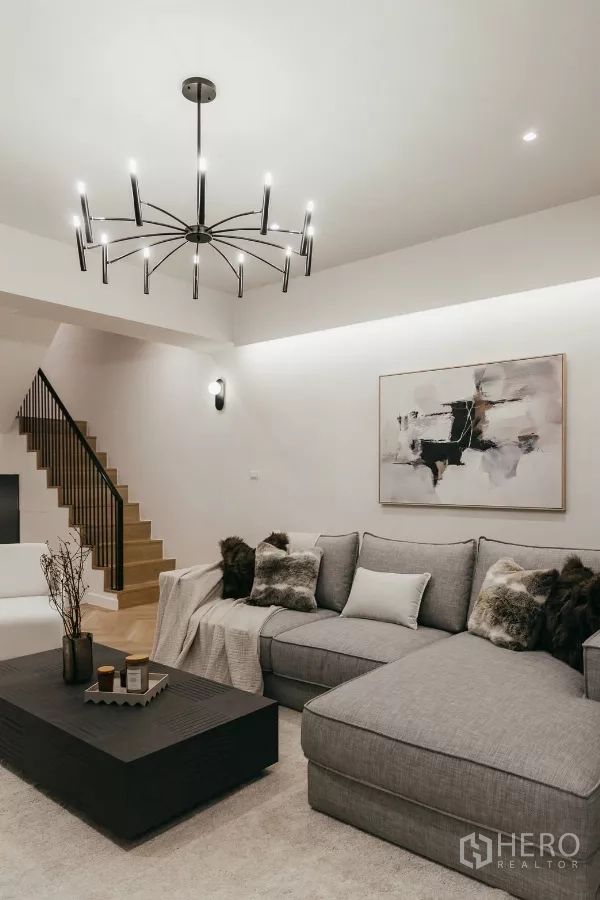 Townhouse for rent in Watthana, Bangkok - Spacious lounge with grey sectional sofa, staircase and contemporary chandelier.