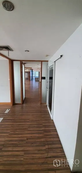 Office Space for rent in Watthana, Bangkok - Office corridor with wood flooring and doorways opening to a light-filled workspace with skyline views.
