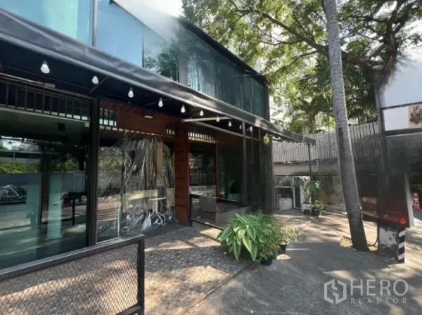 Retail Space for rent in Watthana, Bangkok - Side view of the glass facade with shaded terrace, string lights, trees, and on-site parking space.