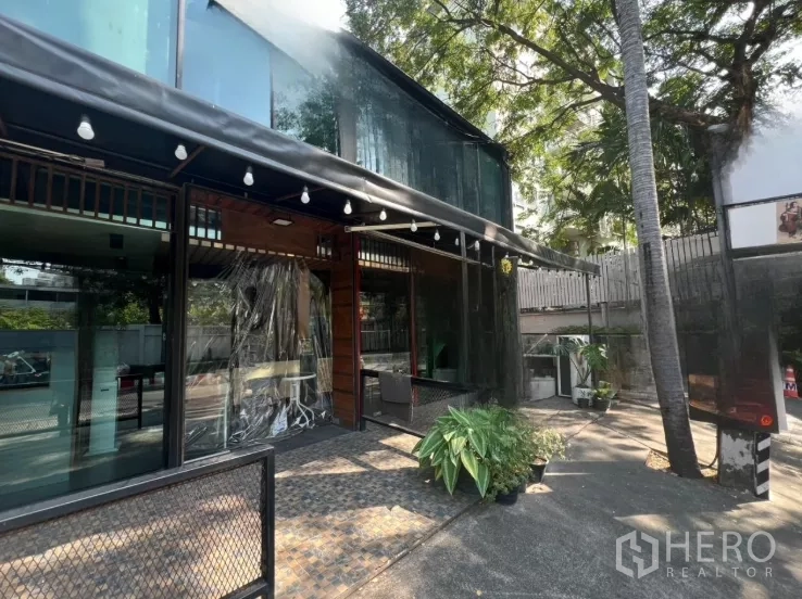 Retail Space for rent in Watthana, Bangkok - Side view of the glass facade with shaded terrace, string lights, trees, and on-site parking space.