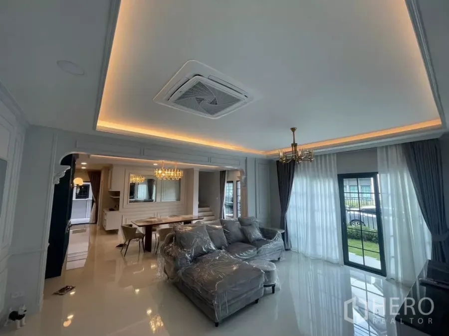 Detached House for rent in Bang Phli, Samut Prakan - Elegant living room with cove lighting, cassette AC, grey sectional sofa and sheer curtains.