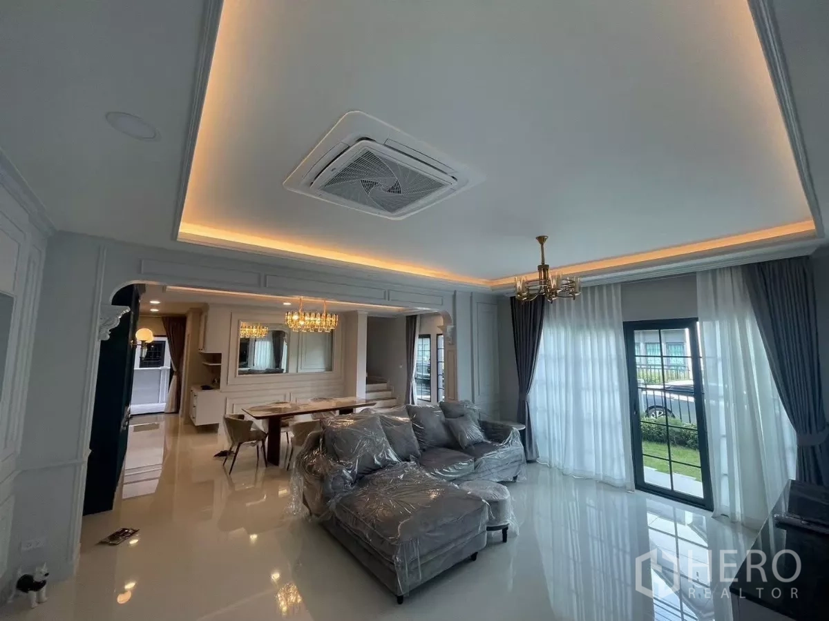 Detached House for rent in Bang Phli, Samut Prakan - Elegant living room with cove lighting, cassette AC, grey sectional sofa and sheer curtains.