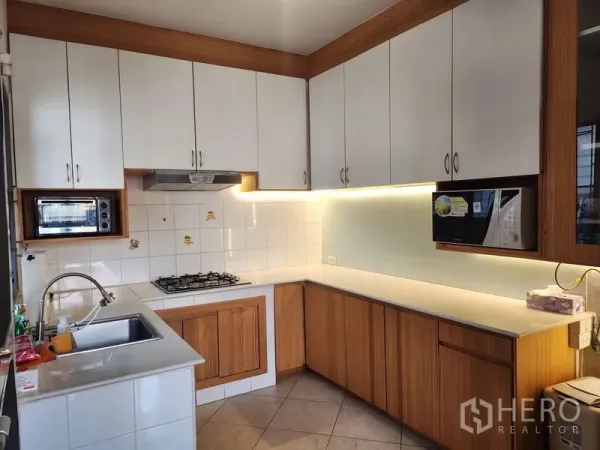 Detached House for rent in Bang Kapi, Bangkok - U-shaped kitchen with white upper cabinets, wood lower cabinets, gas hob and under-cabinet lighting.