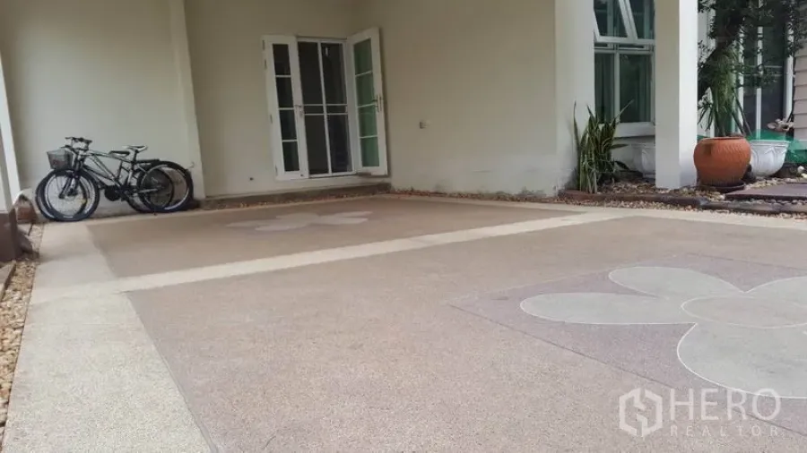 Detached House for sale in Mueang Nonthaburi, Nonthaburi - Covered carport with patterned concrete floor, bicycles, and glass French doors into the house.