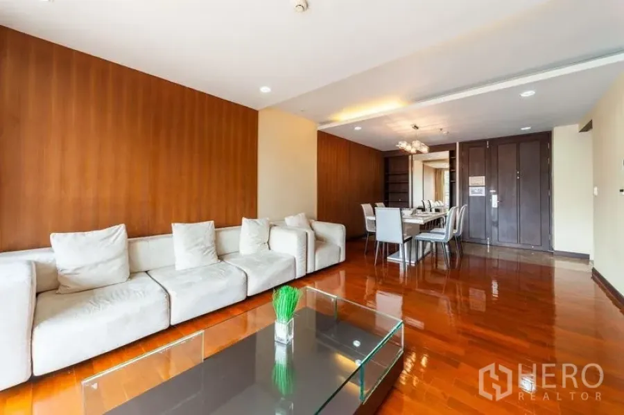 Condominium for rent in Watthana, Bangkok - Open-plan living and dining room with sofa, wood floors, and a large dining table.