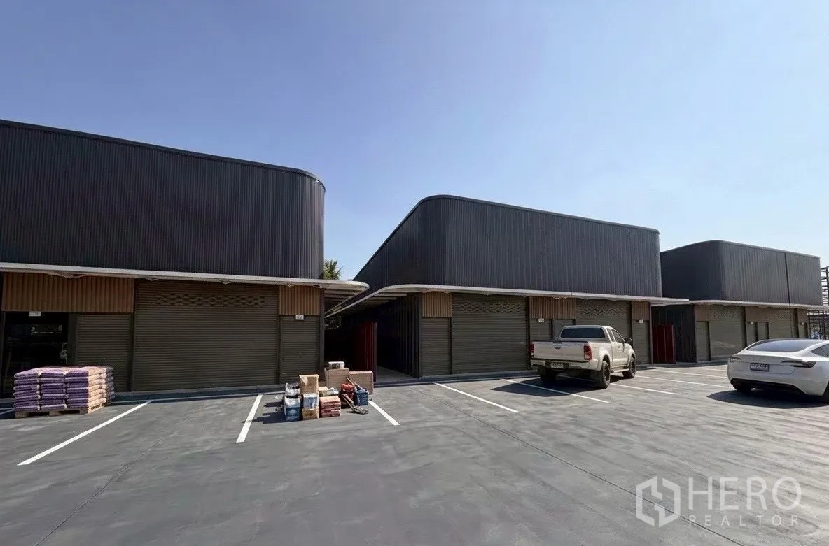 Warehouse for rent in Suan Luang, Bangkok - Warehouse complex frontage with marked parking spaces and vehicles in a paved lot.