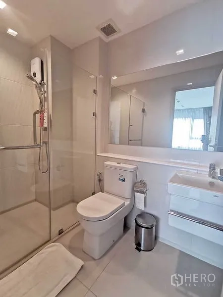 Condominium for rent in Pathum Wan, Bangkok - Contemporary bathroom with glass shower, toilet and vanity.