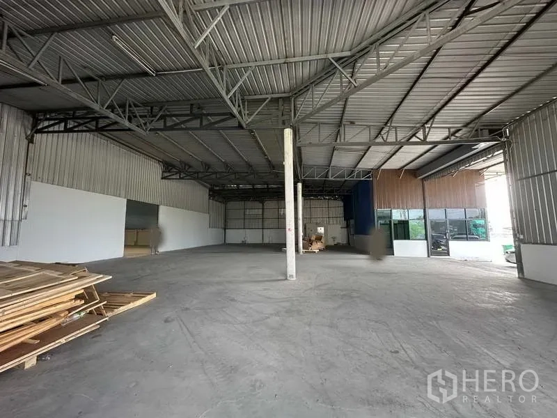 Warehouse for rent in Khlong Luang, Pathum Thani - Spacious warehouse interior with high steel truss roof and attached glass-front office.
