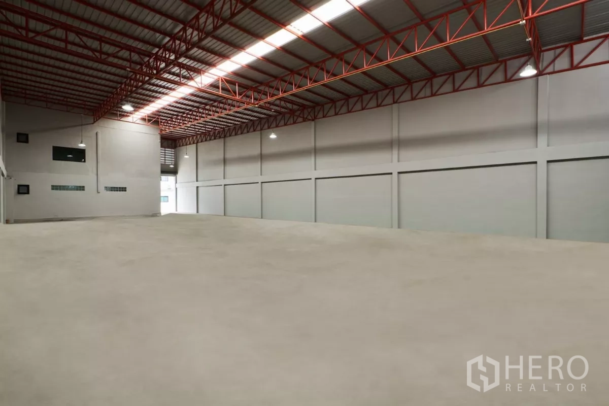 Factory for rent in Mueang Samut Sakhon, Samut Sakhon - Angled view of clean warehouse floor with hanging industrial lights and red trusses.