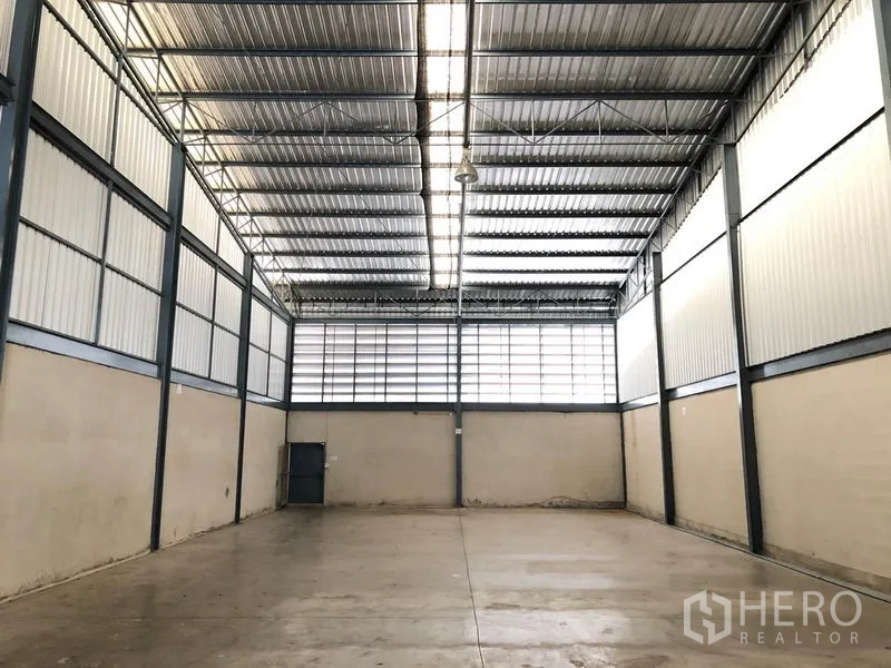 Warehouse for rent in Mueang Samut Prakan, Samut Prakan - Spacious warehouse interior with high steel truss roof, skylight panels and concrete floor.
