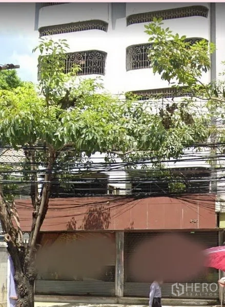 Shophouse for rent in Watthana, Bangkok - Street-facing facade of a multi-storey shophouse with shuttered shopfront and trees.