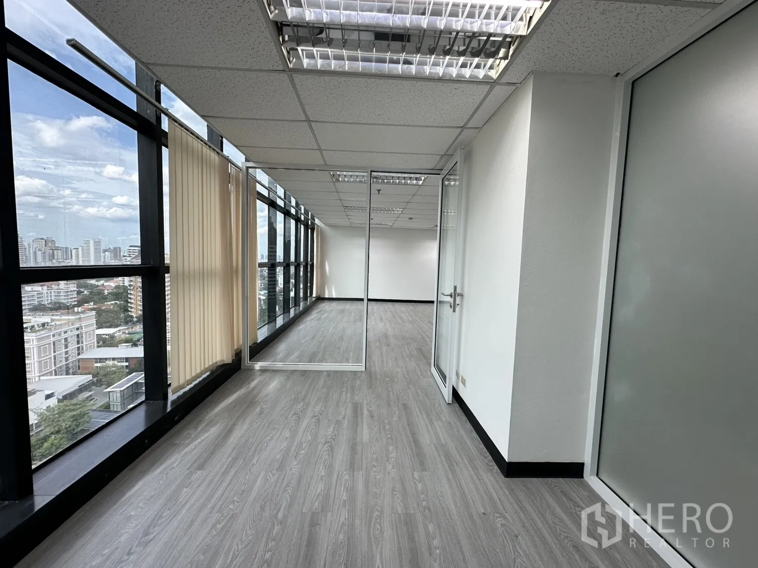 Office Space for rent in Watthana, Bangkok - Window-lined corridor with vertical blinds leading to a glass-door meeting room and city views.