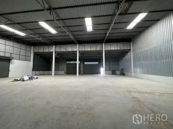 Warehouse for rent in Khlong Luang, Pathum Thani - Open warehouse hall showing roller shutter doors, high ceiling, and bright skylight panels.