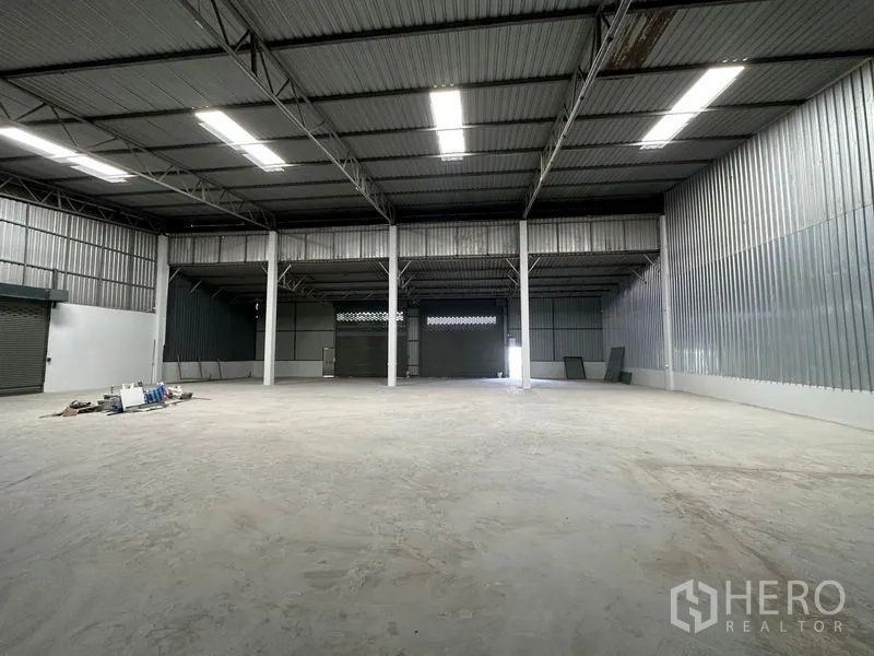 Warehouse for rent in Khlong Luang, Pathum Thani - Open warehouse hall showing roller shutter doors, high ceiling, and bright skylight panels.